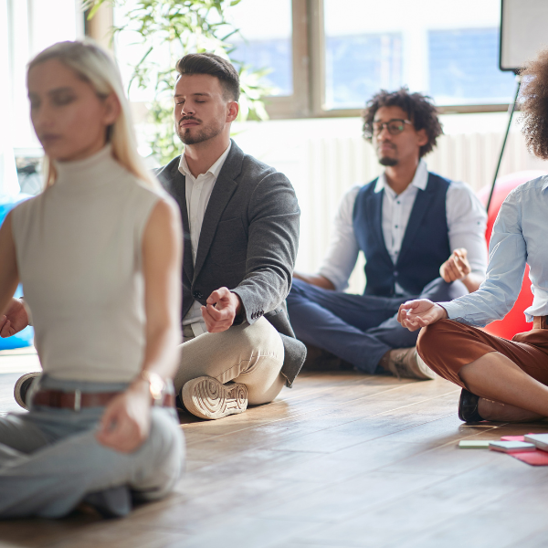 Group of people meditating in a modern office setting, that is kitted out as a wellness space