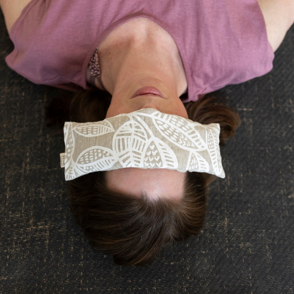 White woman in pink top laying with a white patterned eye pillow over their eyes on a jute eco-friendly yoga mat - taking time out in the office