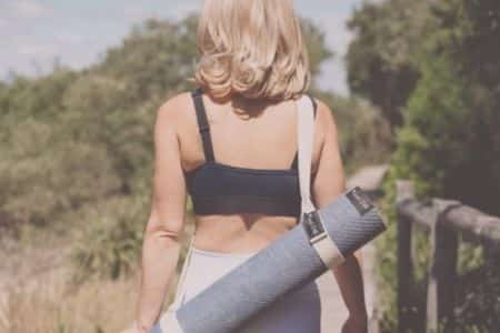 Woman carrying best yoga mat Australia rolled up in blue