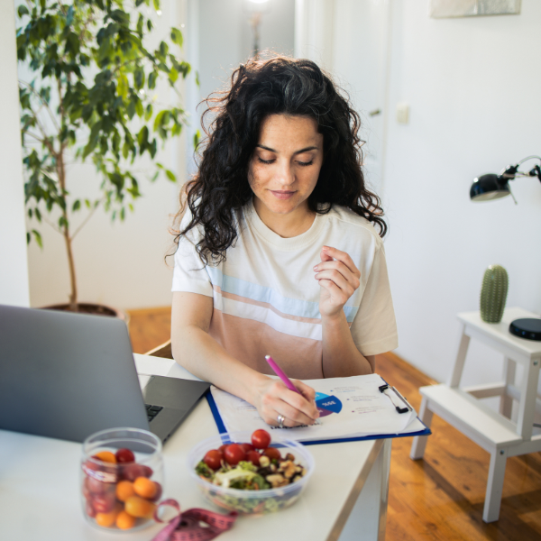 Woman with laptop at a table taking notes during online personalised wellbeing consultation sesson