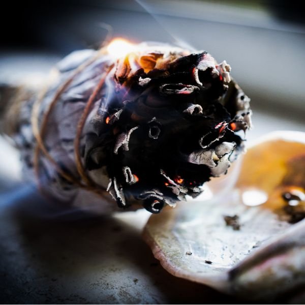 Partially burnt smudge stick that is lying in an Abalone Shell, smoking as part of a cleansing and purifying tirual