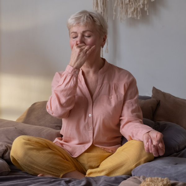 Person sitting on a couch wearing a pink shirt and yellow pants, with a neutral background practising alternative nostril breathing -  - one of the  tips from her personalised wellbeing consultation sesson