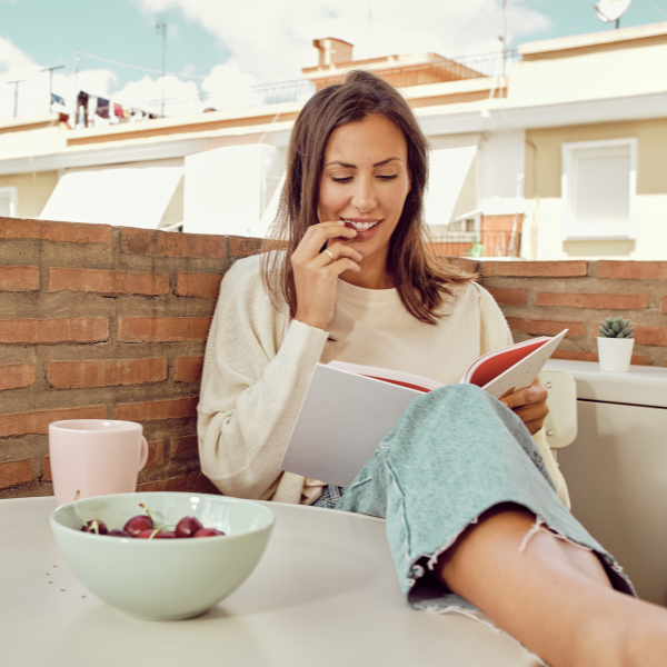 Woman reading a book on a rooftop with a bowl of fruit and a cup -  - one of the  tips from her personalised wellbeing consultation sesson