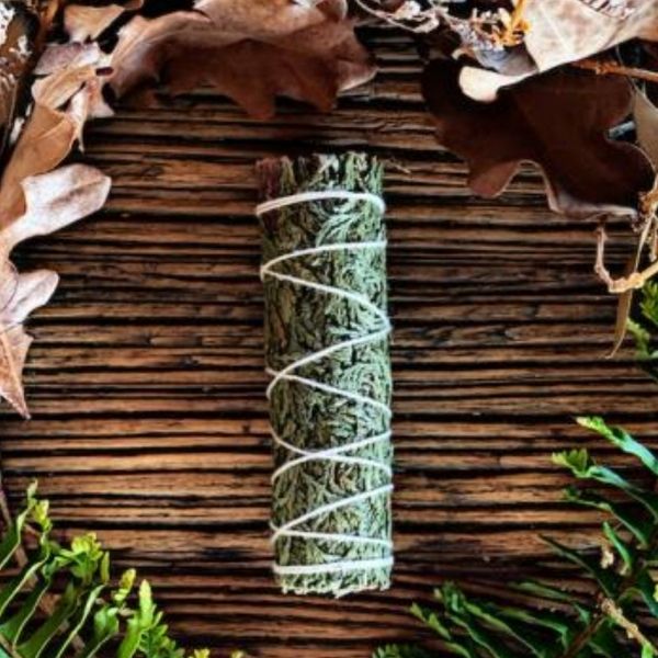 Small cedar smudge stick on a wooden table surrounded by leaves