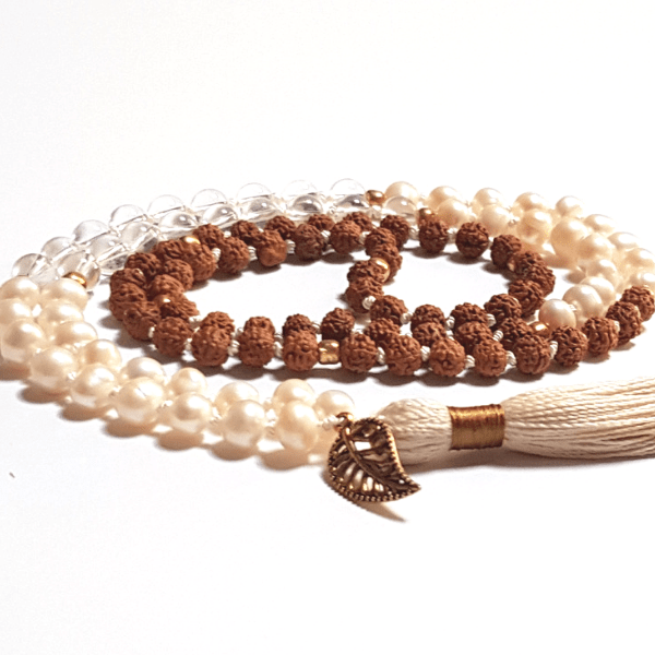 Close up of chndmade Pearl, Quartz and Rudraksha Mala necklace with leaf charm on tassel curled on the table