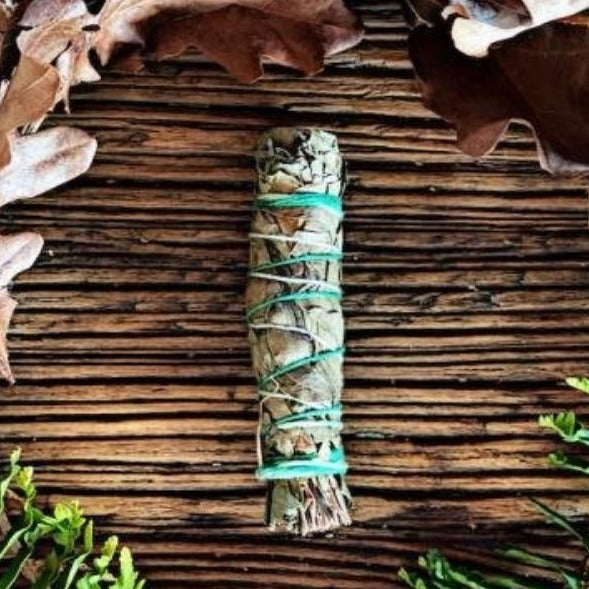 Handmade Eucalyptus smudge stick on wooden table surrounded by leaves 