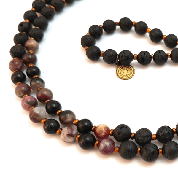 Close up of handmade lava and mixed Tourmaline Mala necklace curled on table