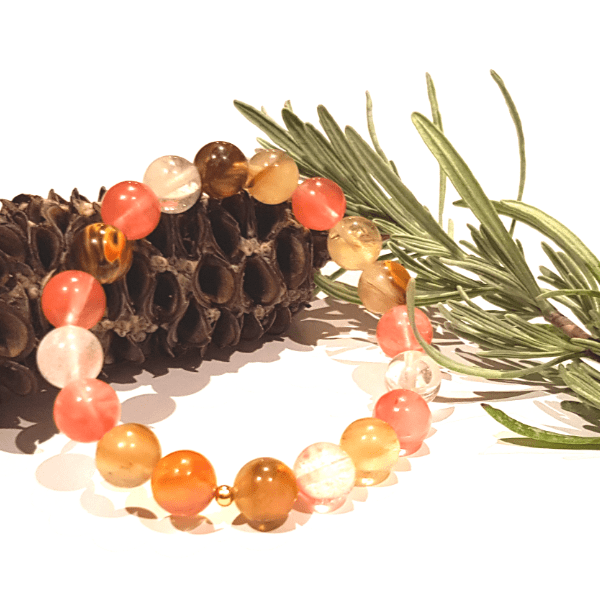 Handmade Light-Hearted Bracelet – Tourmalinated Quartz Bracelet for Positivity on white background laid on pine cone with Rosemary in background