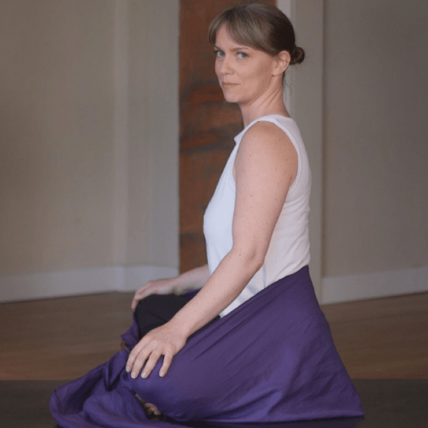 Woman sitting crossed legged with a purple lotus meditation wrap wrapped around her legs and hips, secured with D ring