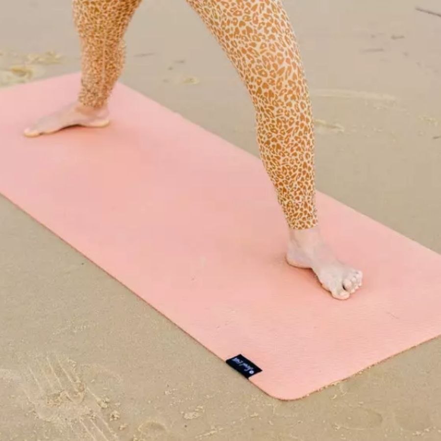 Woman on beach standing in warrior pose on pink clay yoga mat