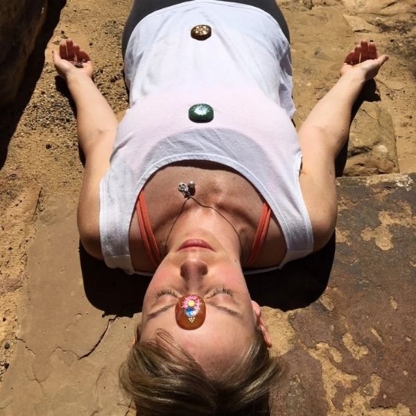 Woman laying on ground with crystal Shavasana Stones laid on chakra points on her body