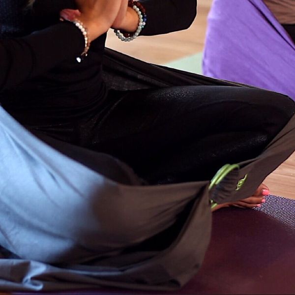 Woman sitting cross legged in meditation with a grey lotus wrap wrapped around her legs and hips secured with a D ring at the front of her legs